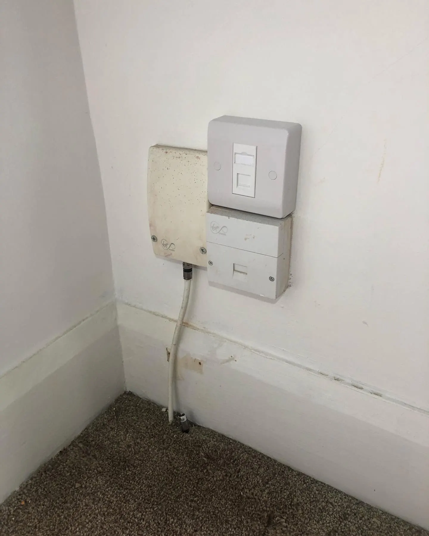 White single network socket in a surface box mounted above a Virgin Media phone socket beside an old coax box