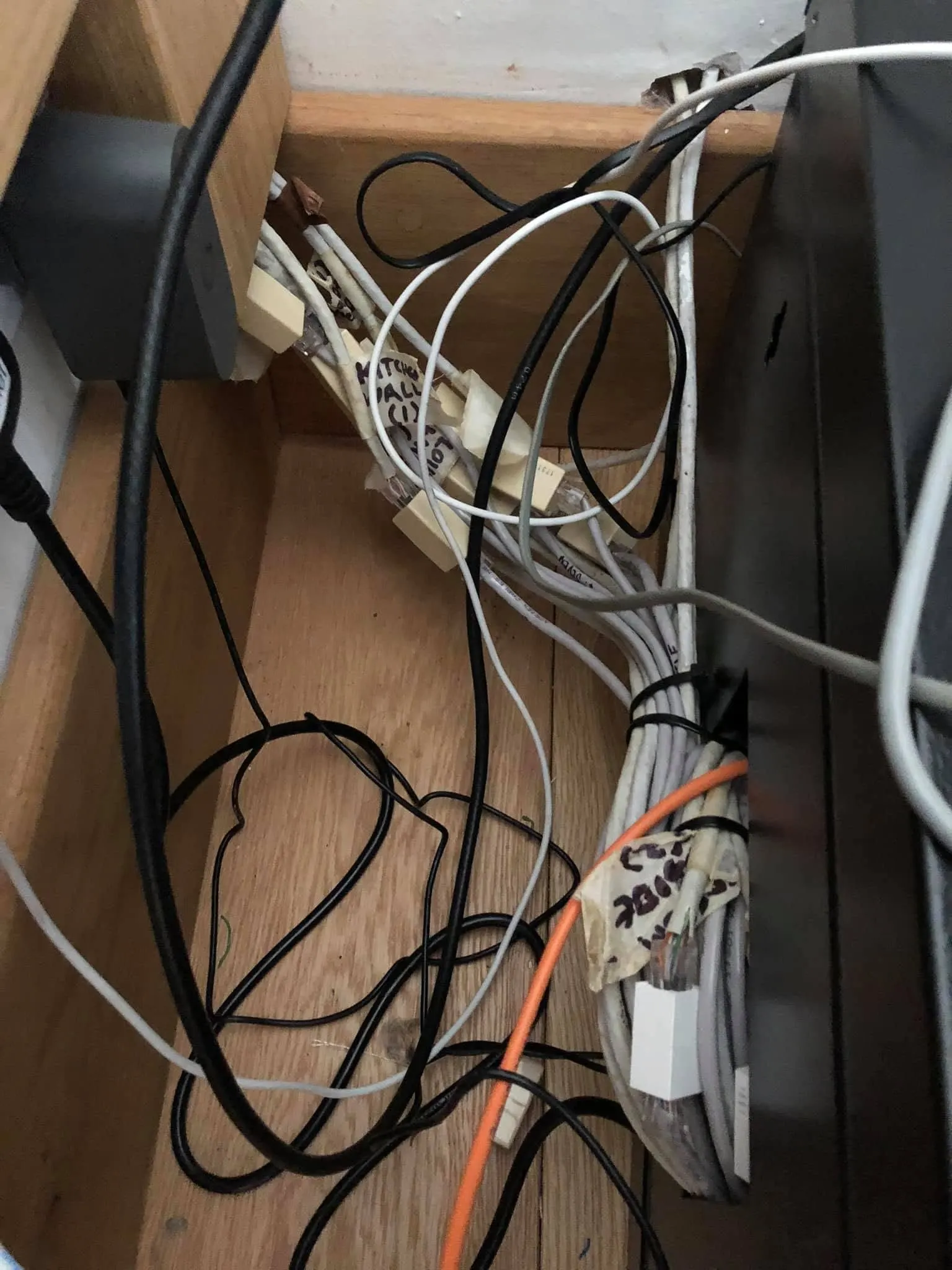 RJ45 couplers held together with masking tape and hand-written labels among loose cables inside a wooden cabinet
