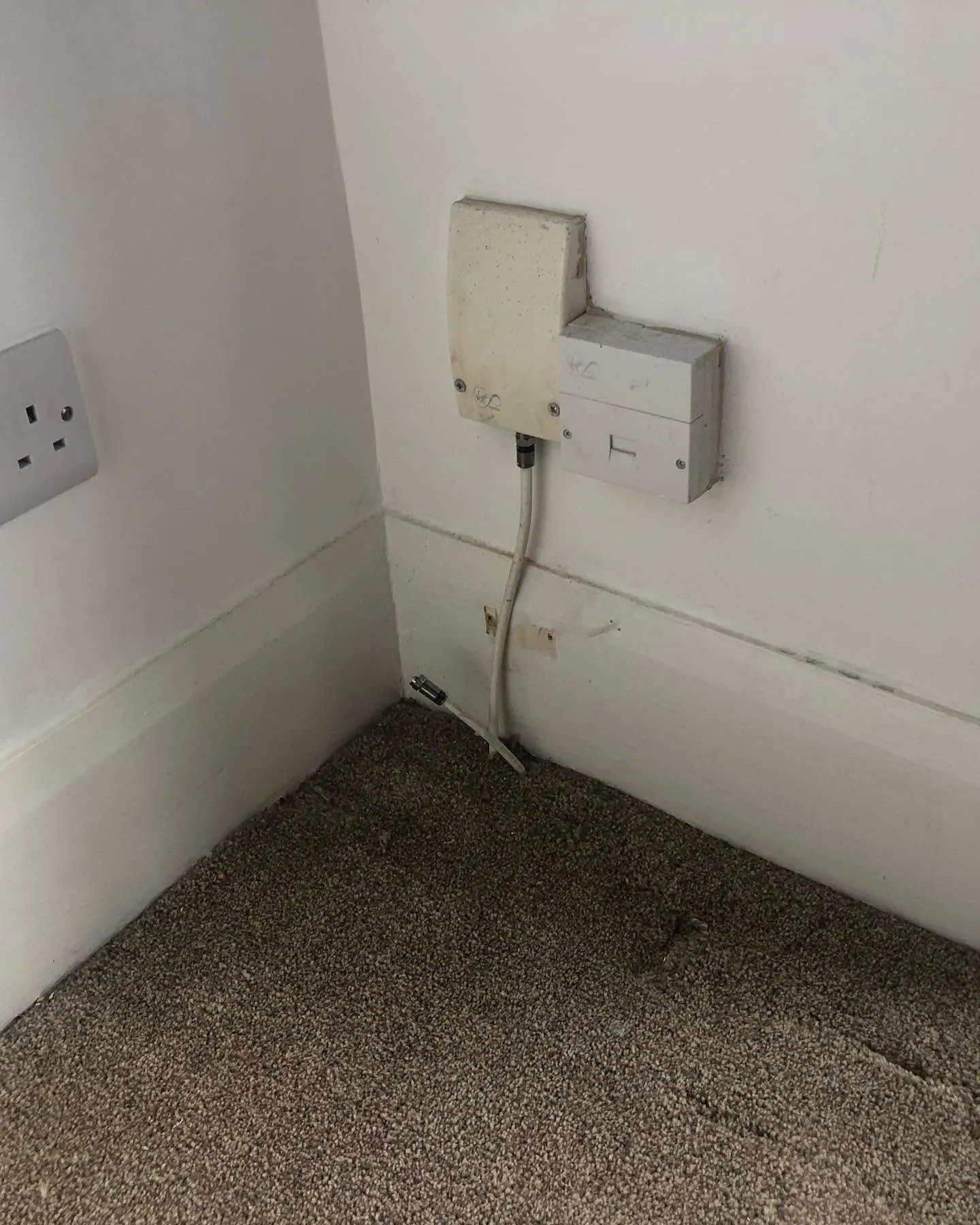 Old yellowed Virgin Media coax box and phone socket in a room corner, with a loose coax lead on the carpet