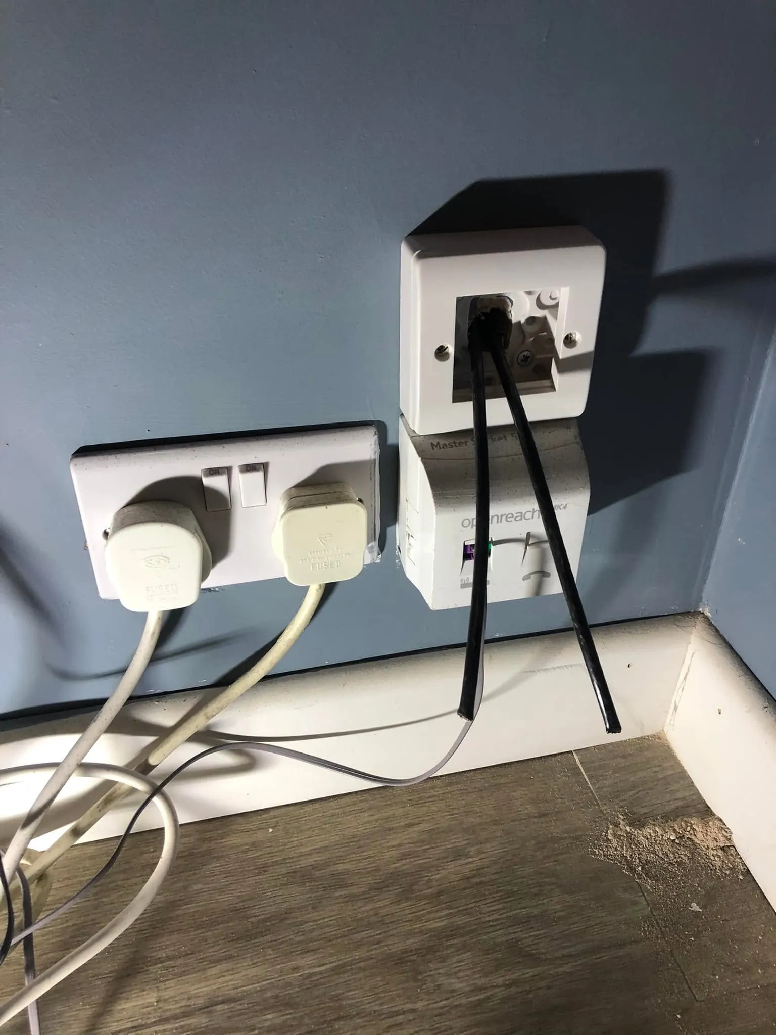 Open back box above an Openreach master socket with two black cables hanging out, next to a double plug socket with two plugs