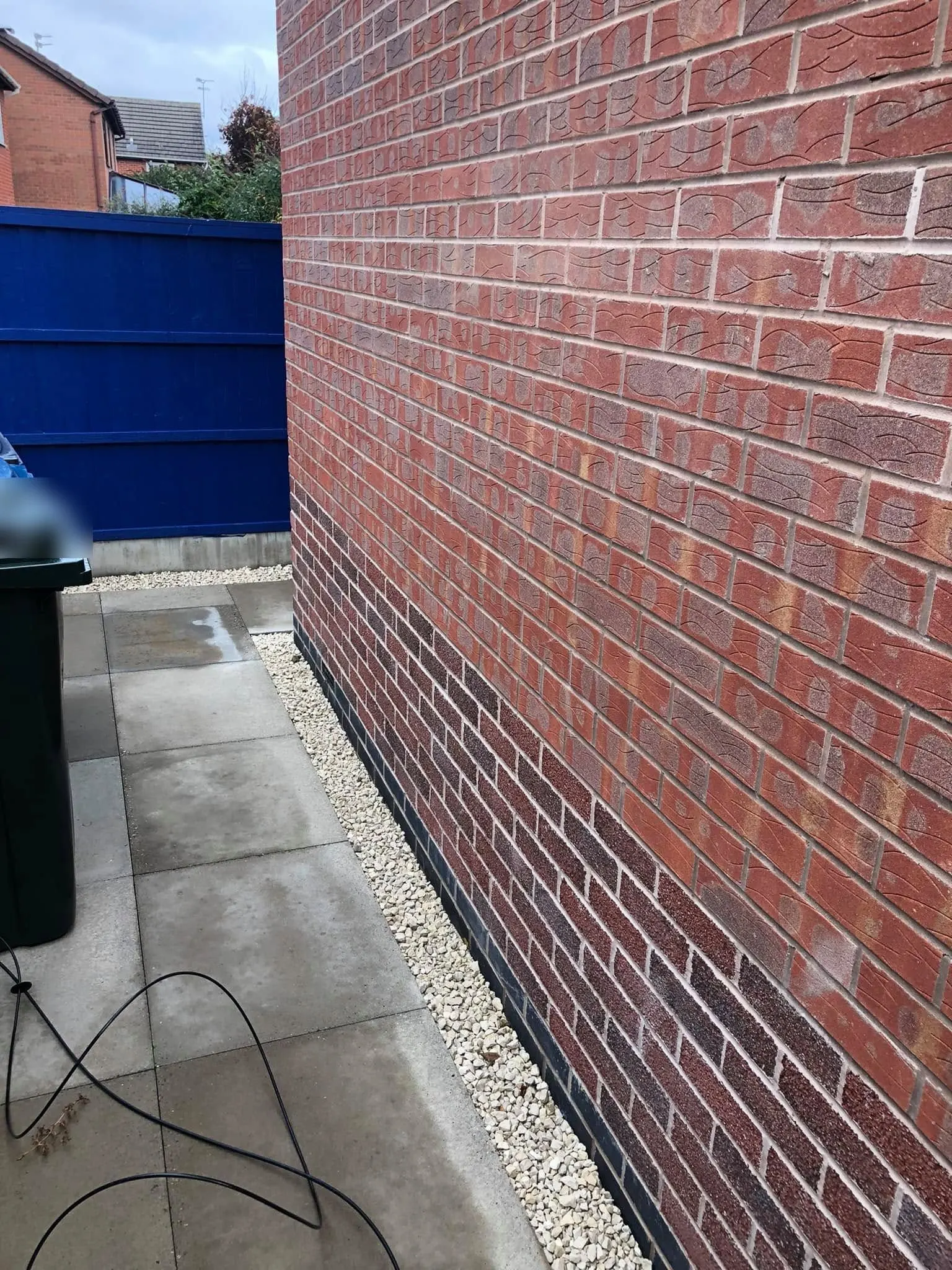 Loose black cable lies in loops on the paving of a side passage between a brick wall and a wheelie bin