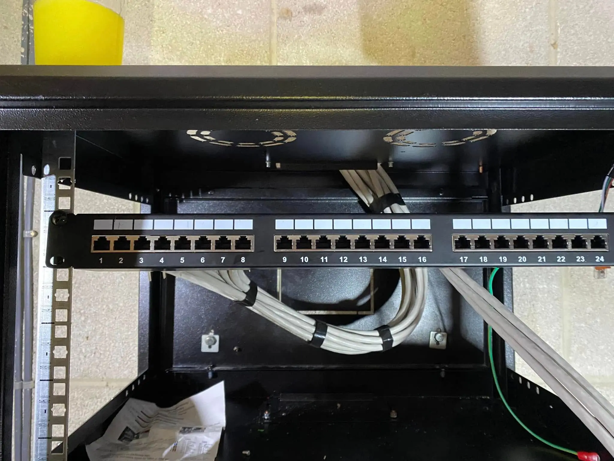 Numbered 24-port patch panel in a black wall cabinet with bundled grey cables looping behind it