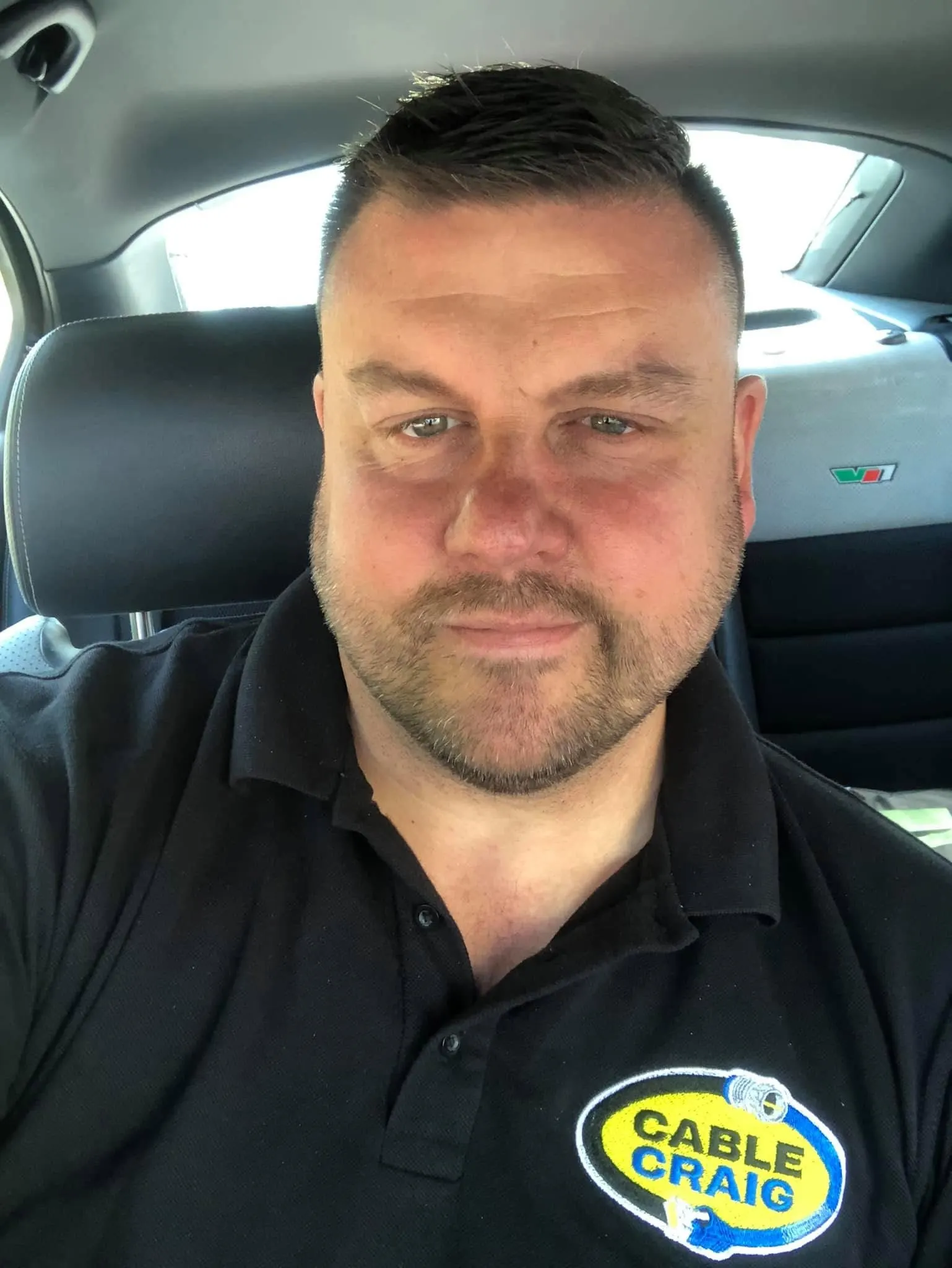 Craig in a black Cable Craig polo, taking a selfie from the driver seat