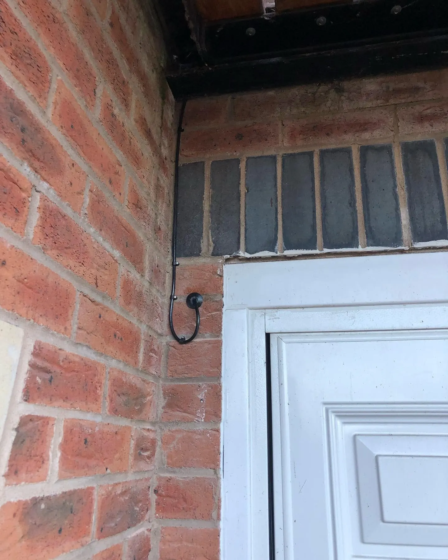 Black cable running down a brick corner from the soffit into a drip loop and grommet beside a white door frame