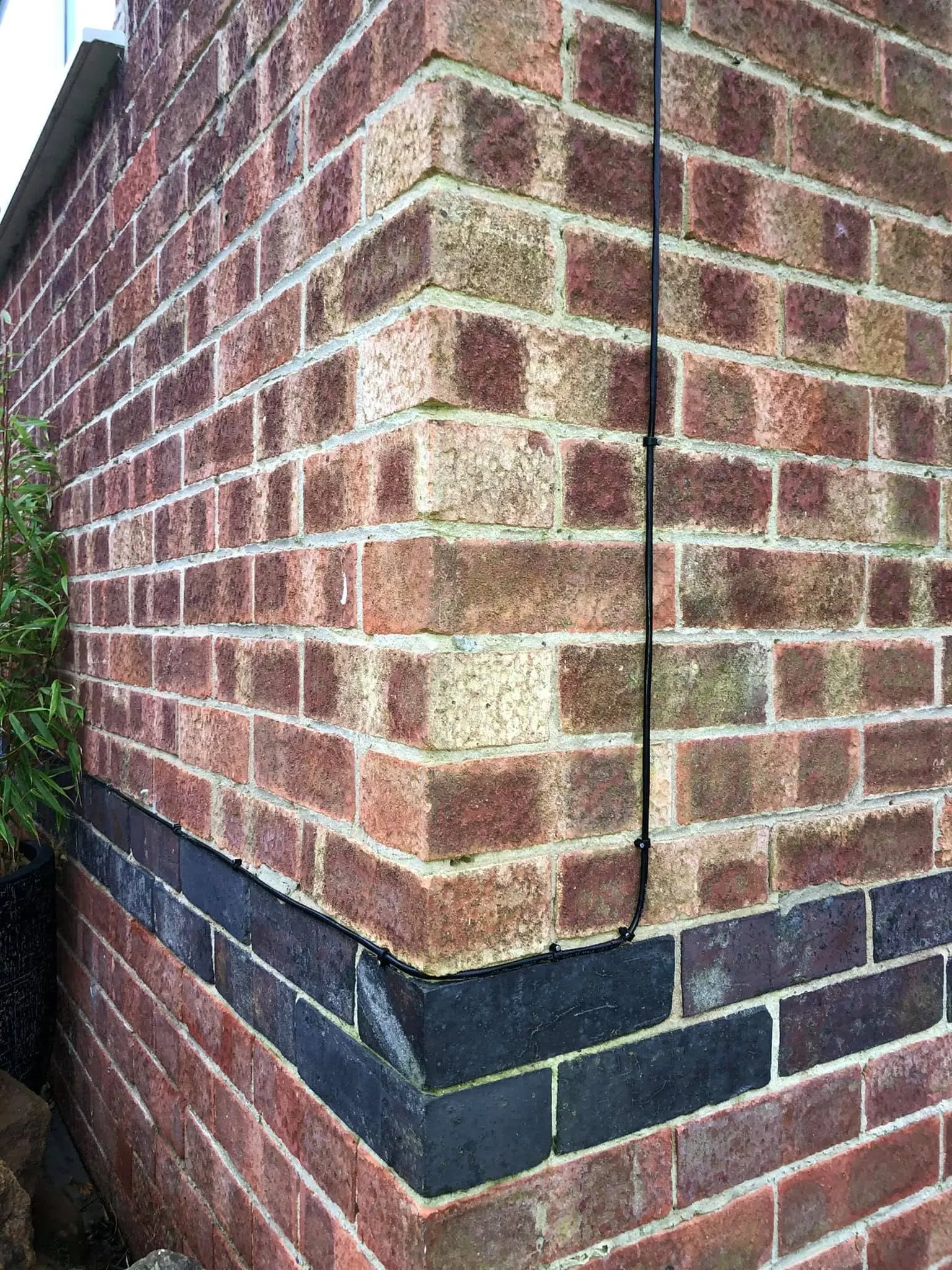 Black cable coming down a red brick corner and turning to follow the top of a blue brick course round the corner