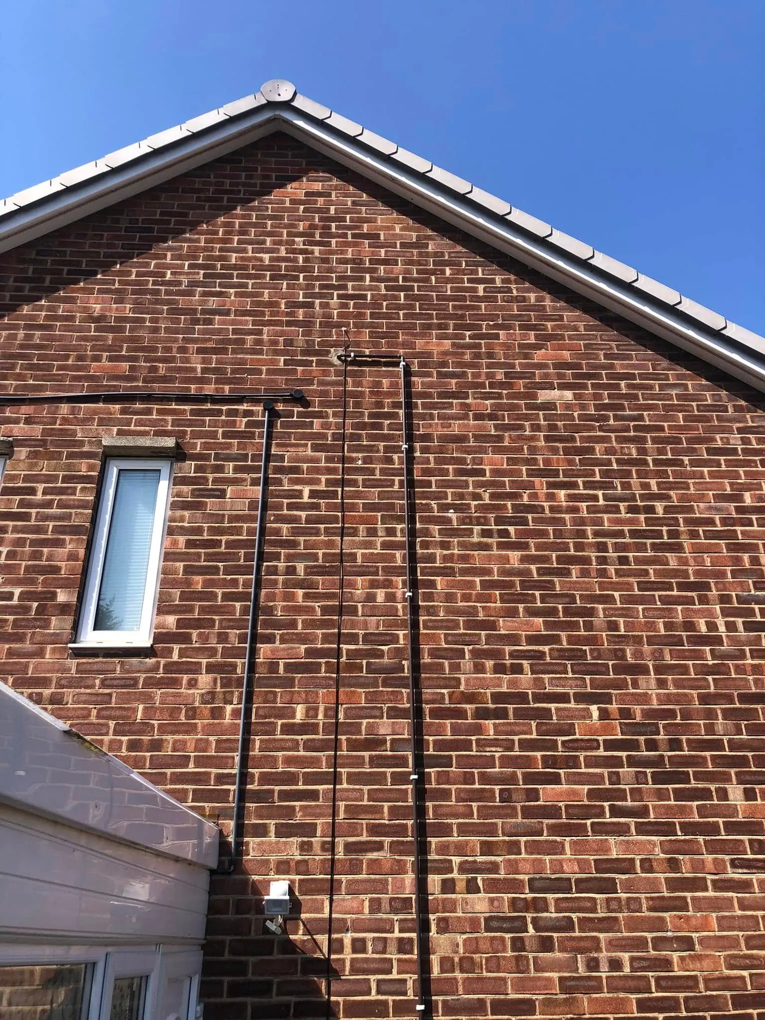 Brick gable end under blue sky with black cables running vertically from near the roof down towards a conservatory