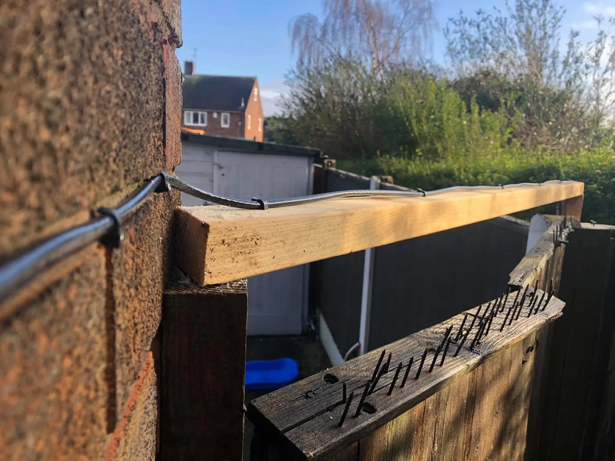 Dark cable clipped along a brick pier and across a new timber rail spanning over a garden fence