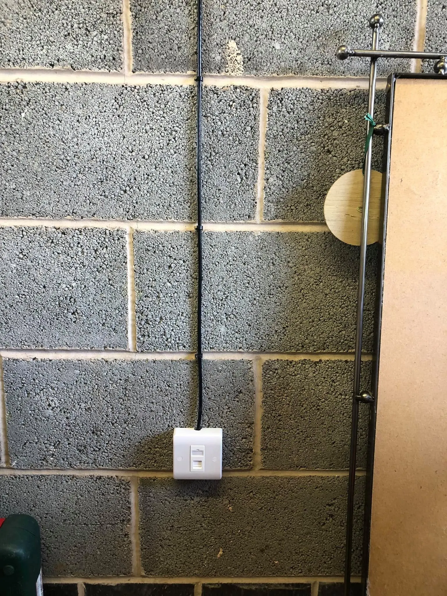 White data faceplate on a grey breeze-block wall with a black cable clipped down to it