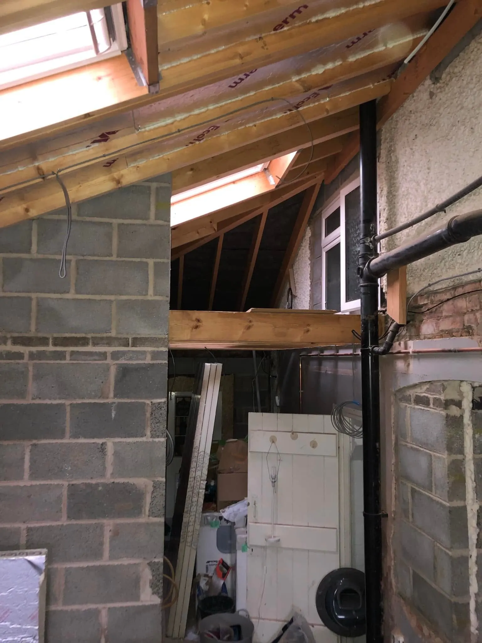 Grey cable clipped along exposed timber rafters in an unfinished extension with block walls and roof windows