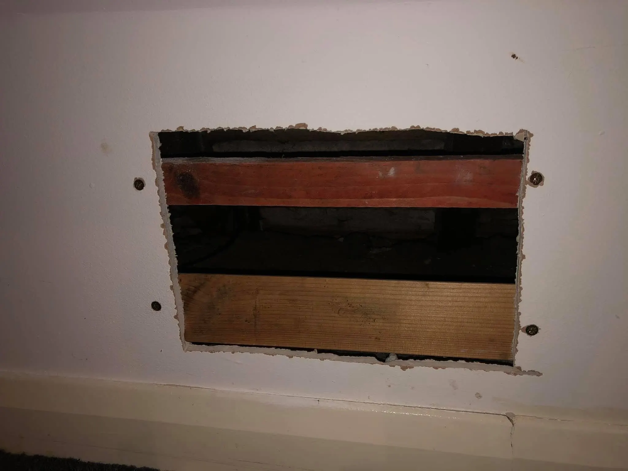 Rectangular hole cut in a plasterboard wall above the skirting board, showing timber noggins in the void behind