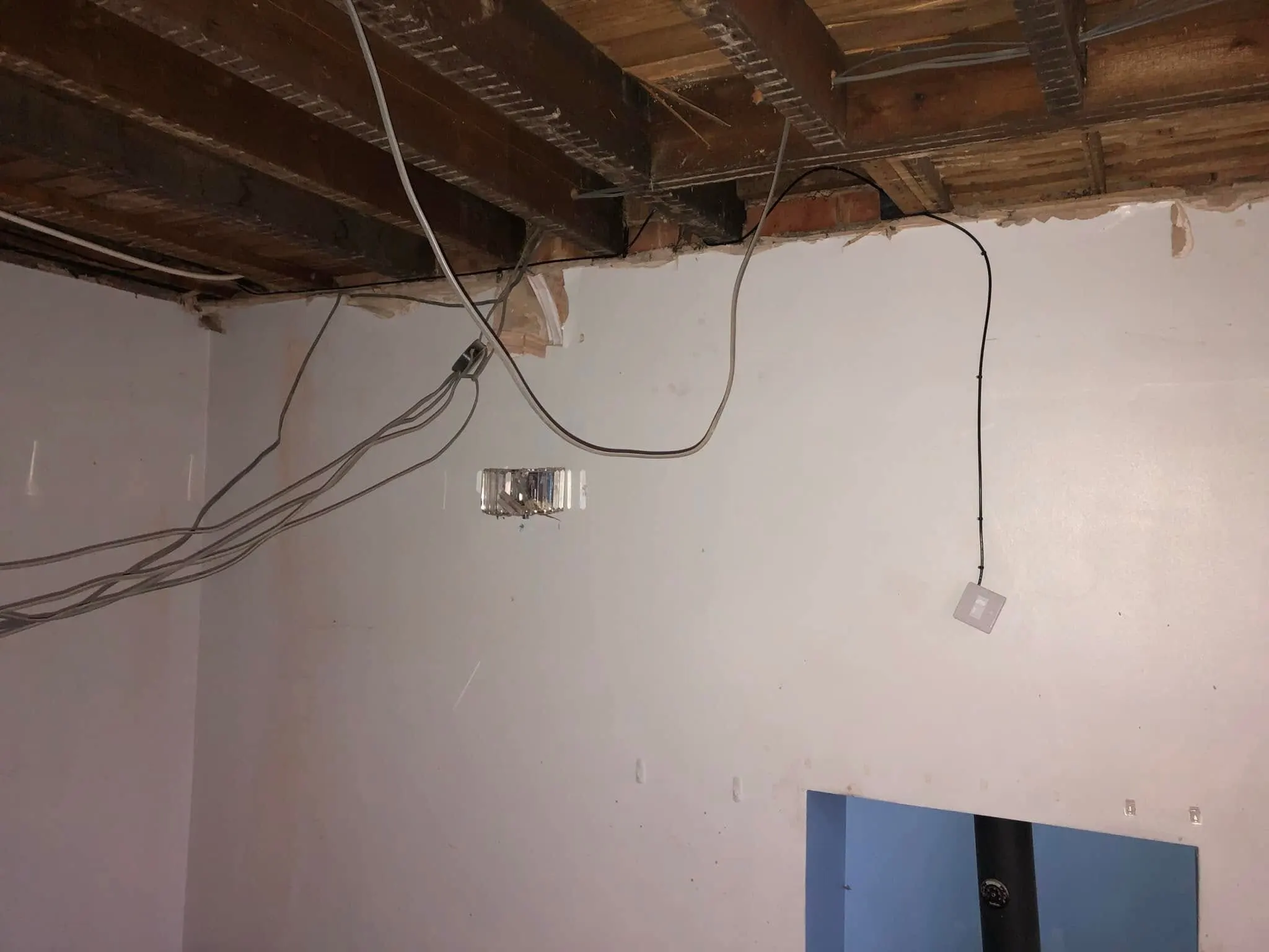 Black cable clipped down a white wall from exposed ceiling joists to a small white faceplate, with grey cables hanging nearby