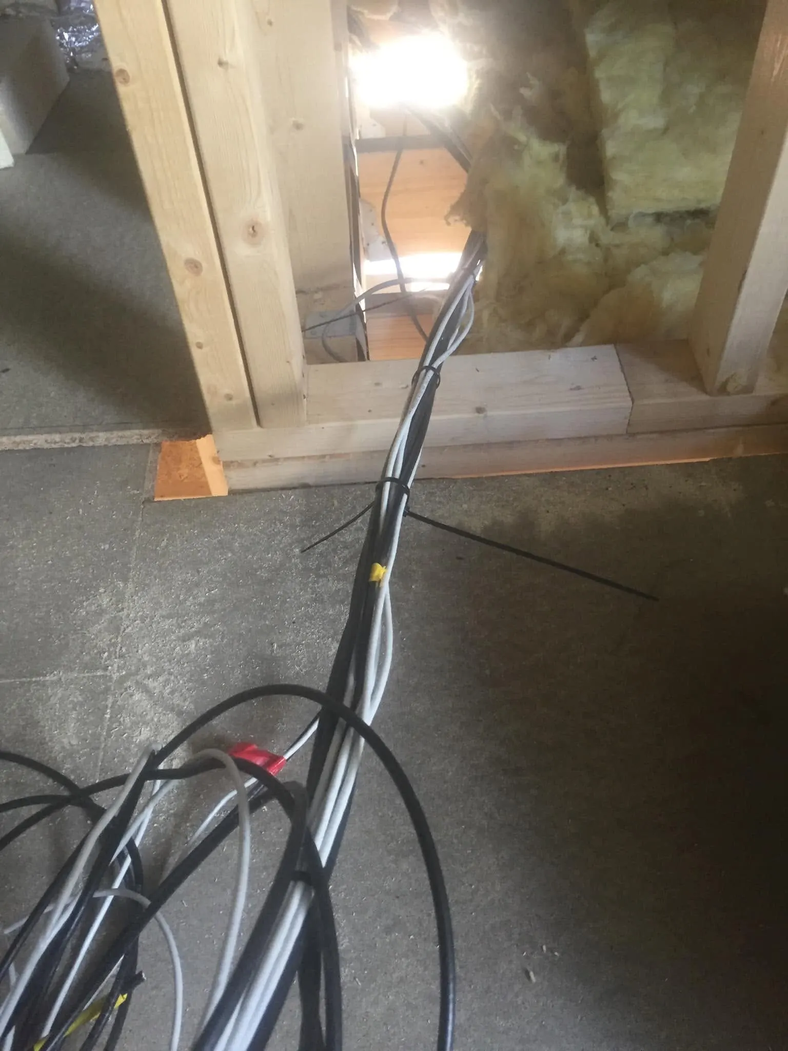 Bundle of black and grey cables cable-tied together, running across a concrete floor into a timber stud wall
