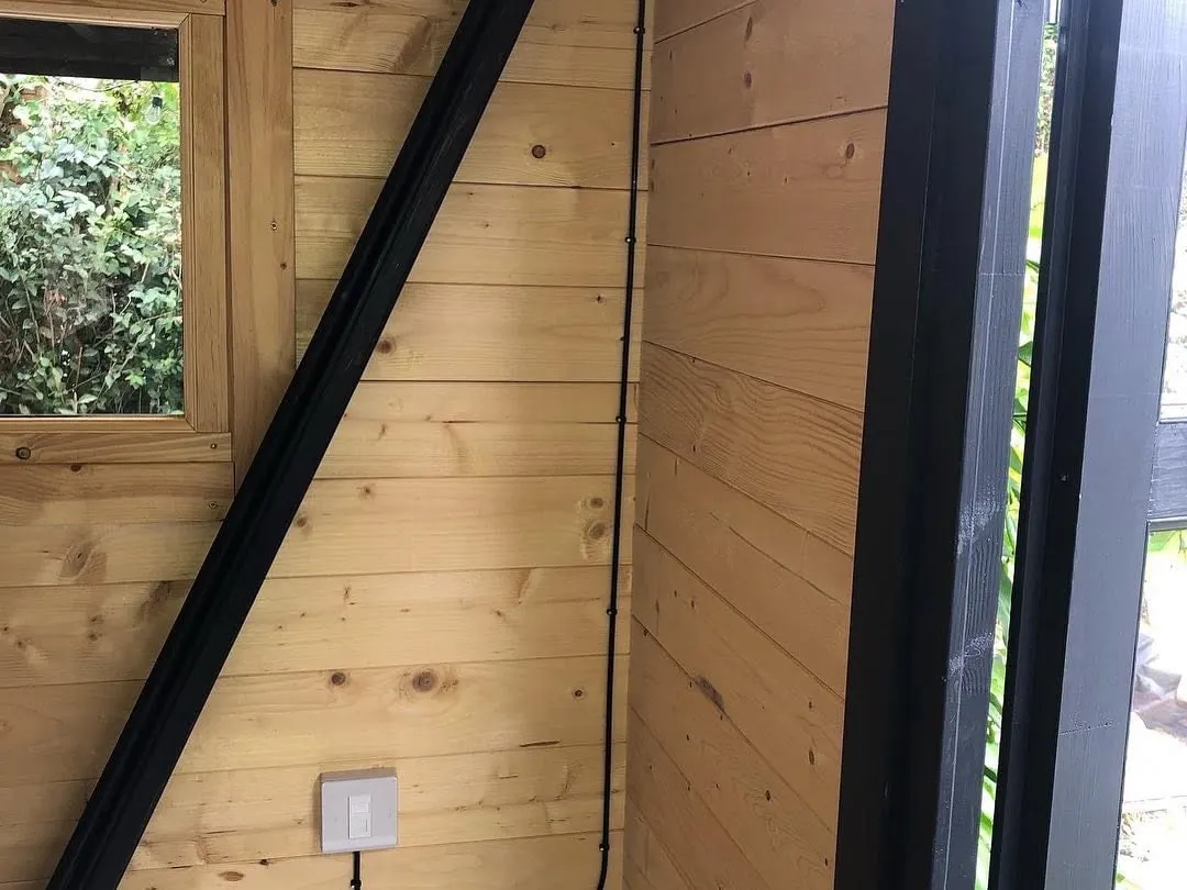 Single white data outlet low on a pine-clad wall, with its black cable clipped up the corner