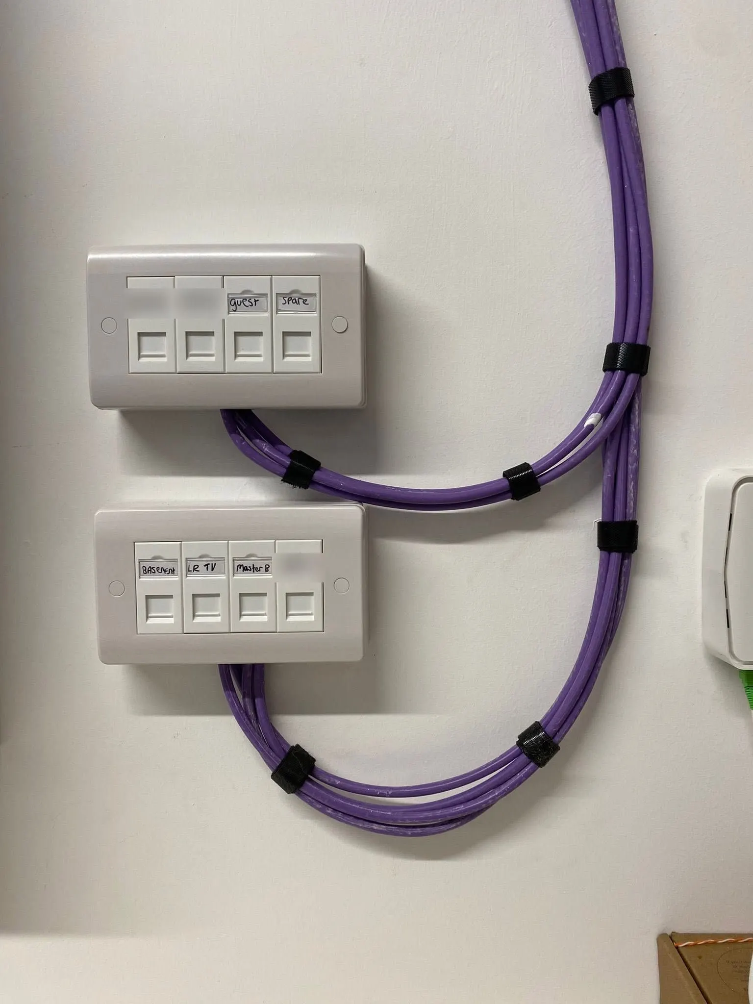 Two four-port data plates with hand-written port labels, purple cables held in neat loops by black velcro straps