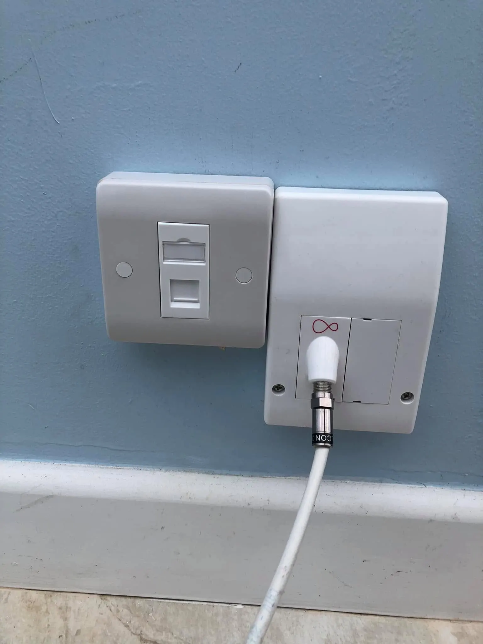 Single ethernet socket mounted beside a Virgin Media wall outlet with a white coax lead, on a pale blue wall