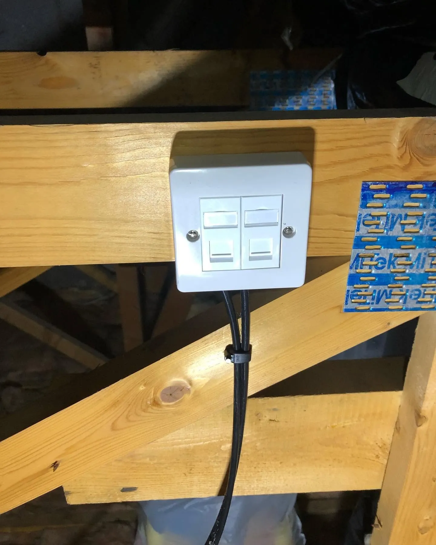 Twin ethernet faceplate on a surface box fixed to a loft roof truss, two black cables clipped below it