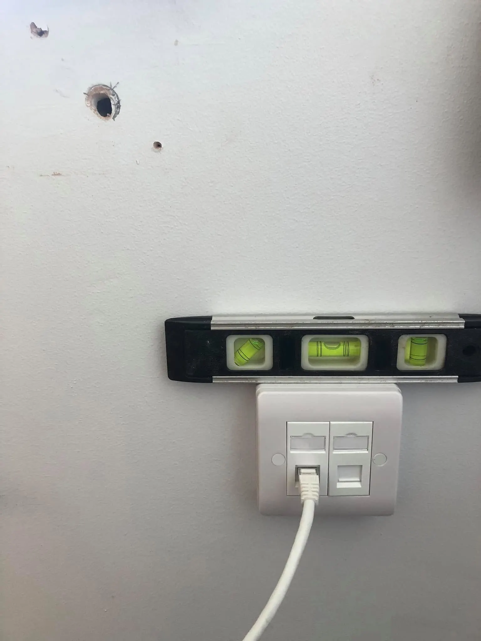 Twin ethernet faceplate with a spirit level resting on top and a white patch lead in the left port
