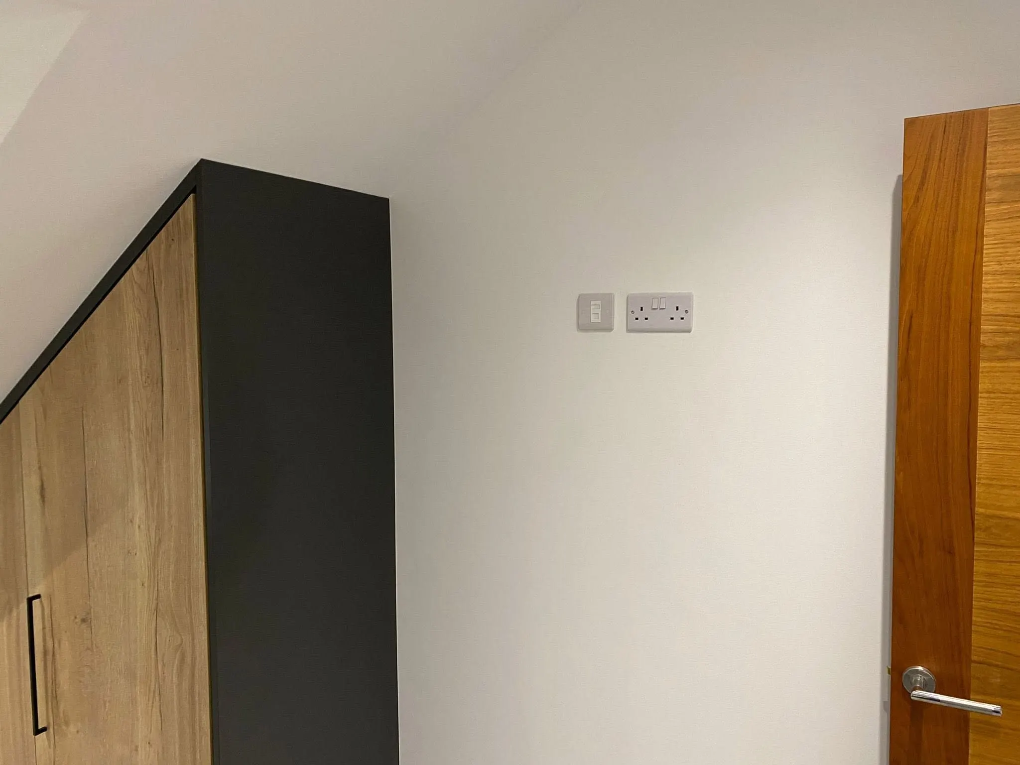 Flush data socket beside a double power socket on a white wall, between an oak-effect wardrobe and a wooden door
