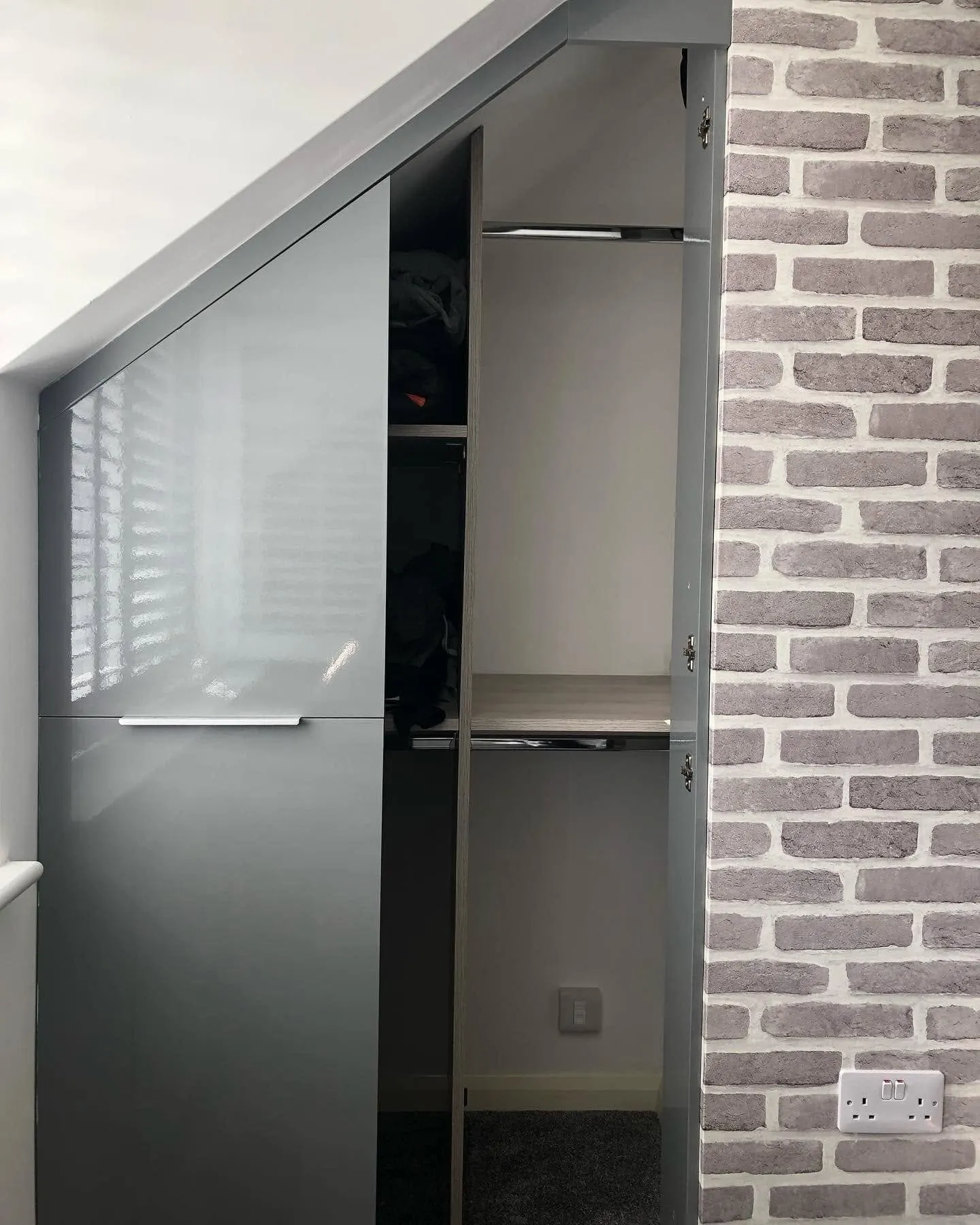 Grey gloss under-eaves wardrobe with its door open, showing a small grey data socket low on the back wall