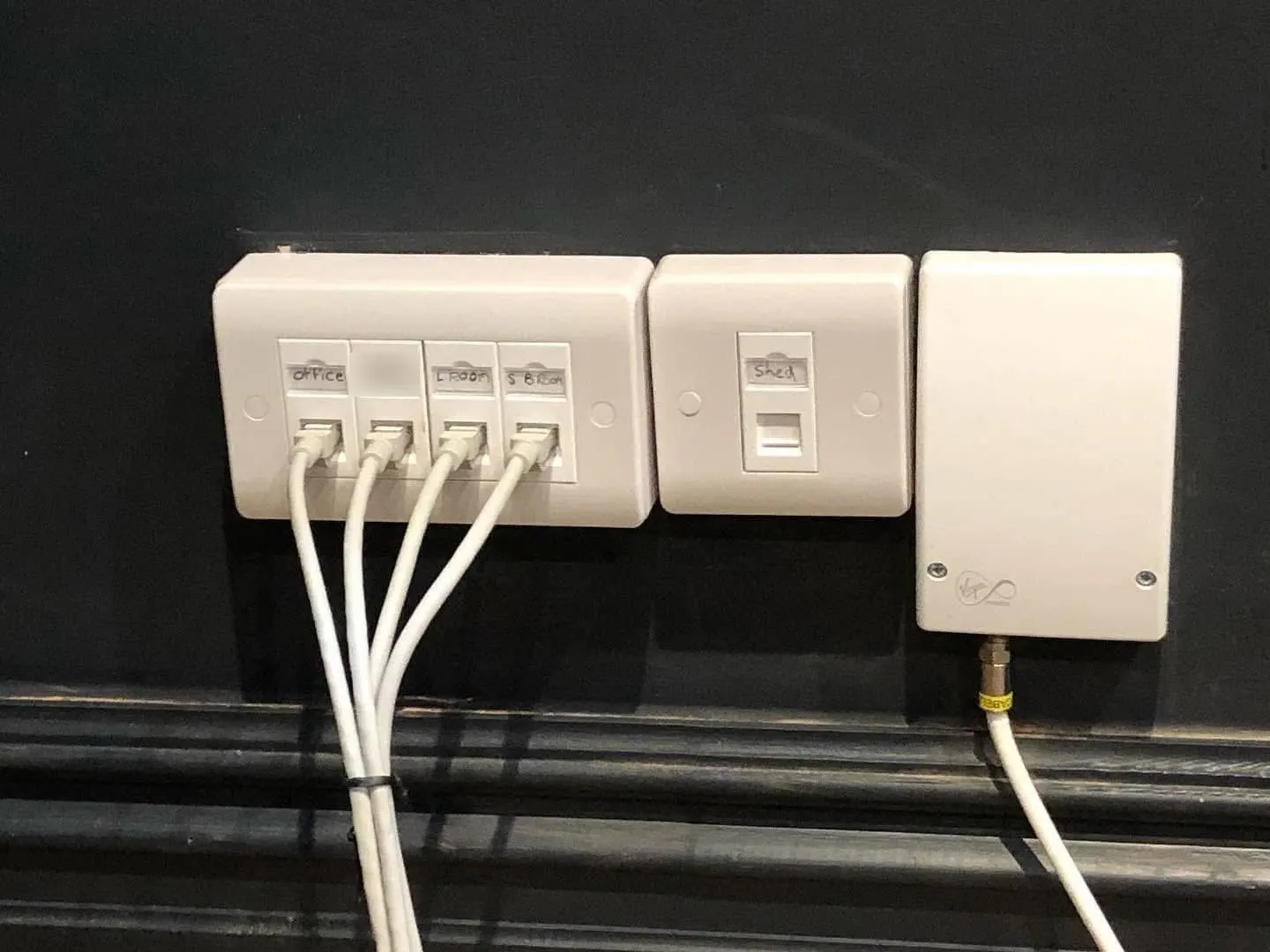 Four-port ethernet faceplate with patch leads, a single port labelled Shed and a Virgin Media wall box on a dark wall