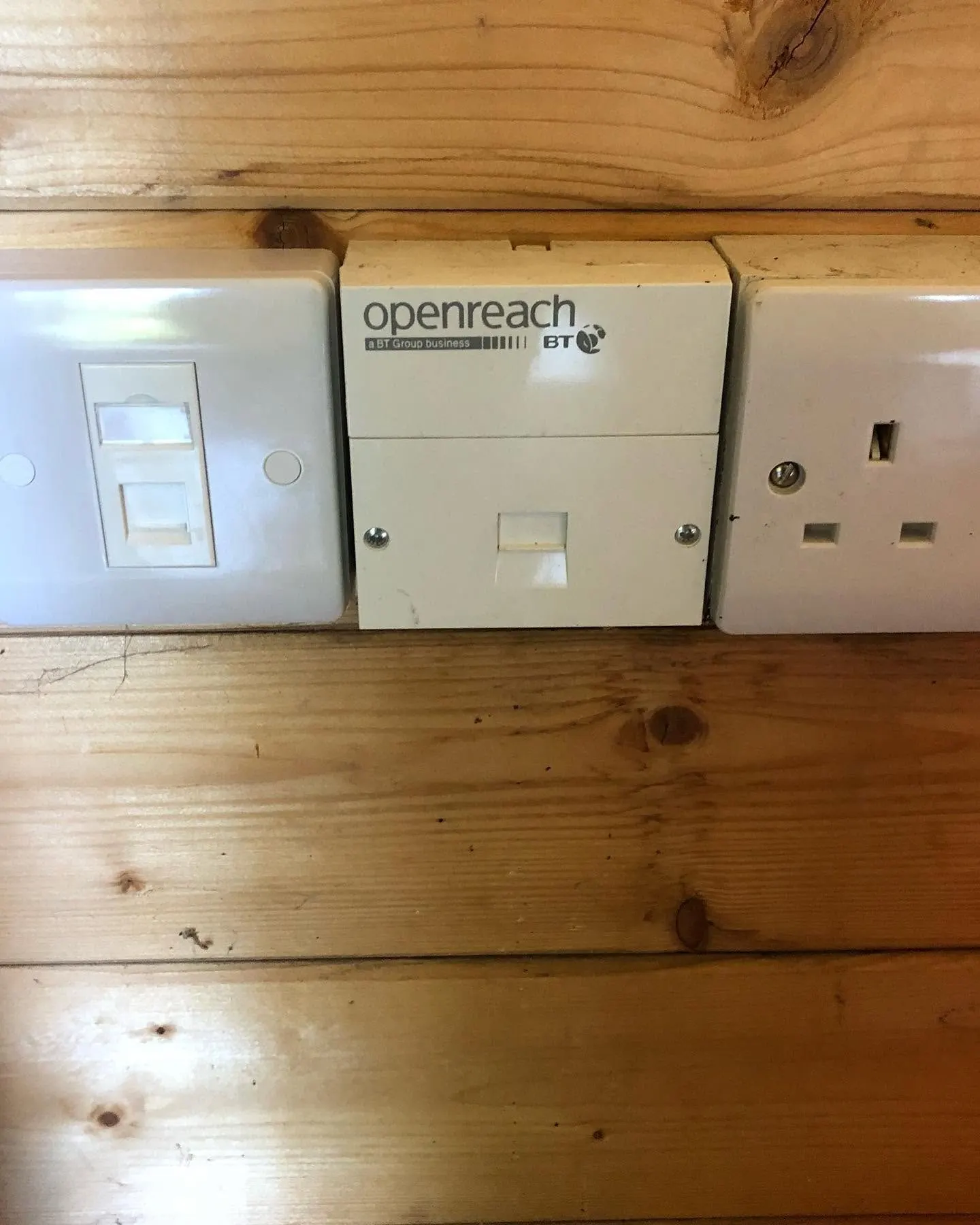 Single ethernet faceplate, an Openreach master socket and a power socket in a row on a log cabin wall