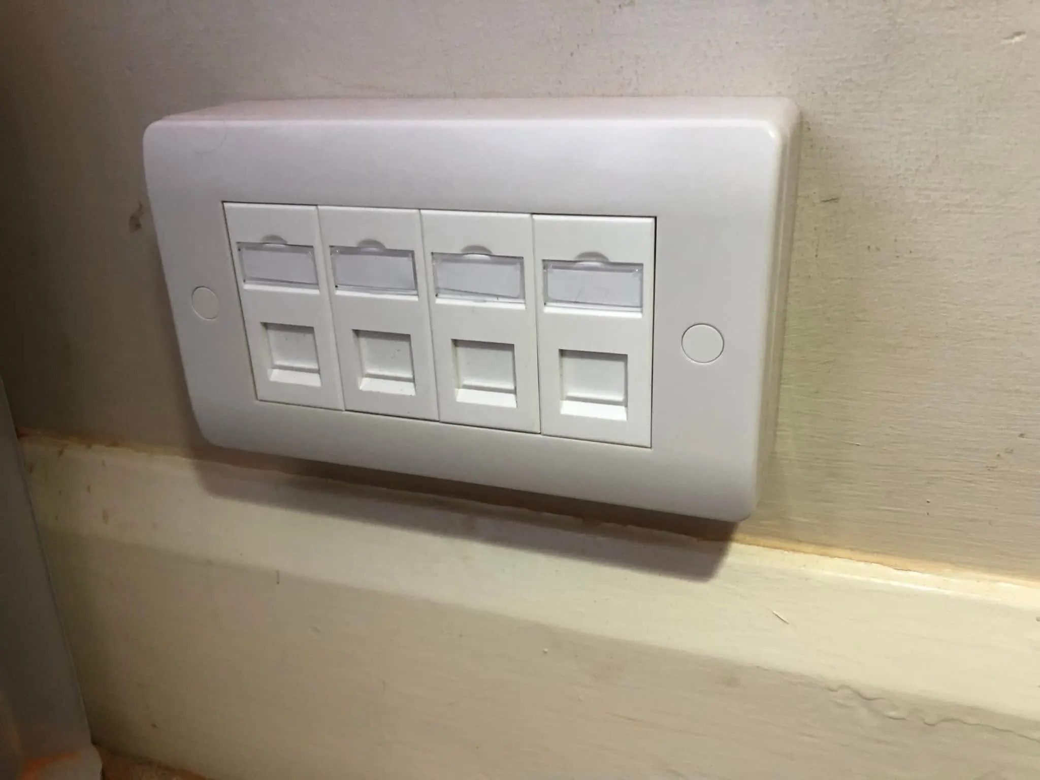 Four-port ethernet faceplate with blank label windows on a surface box just above a skirting board