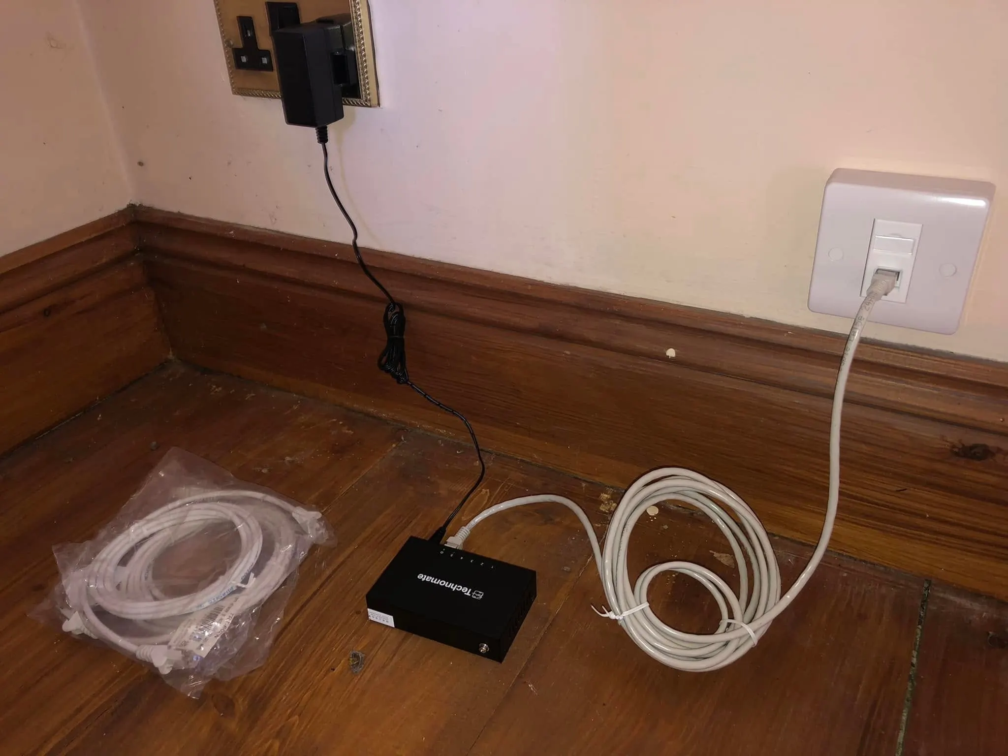 Technomate network switch on floorboards, patched to a white data outlet above the skirting board