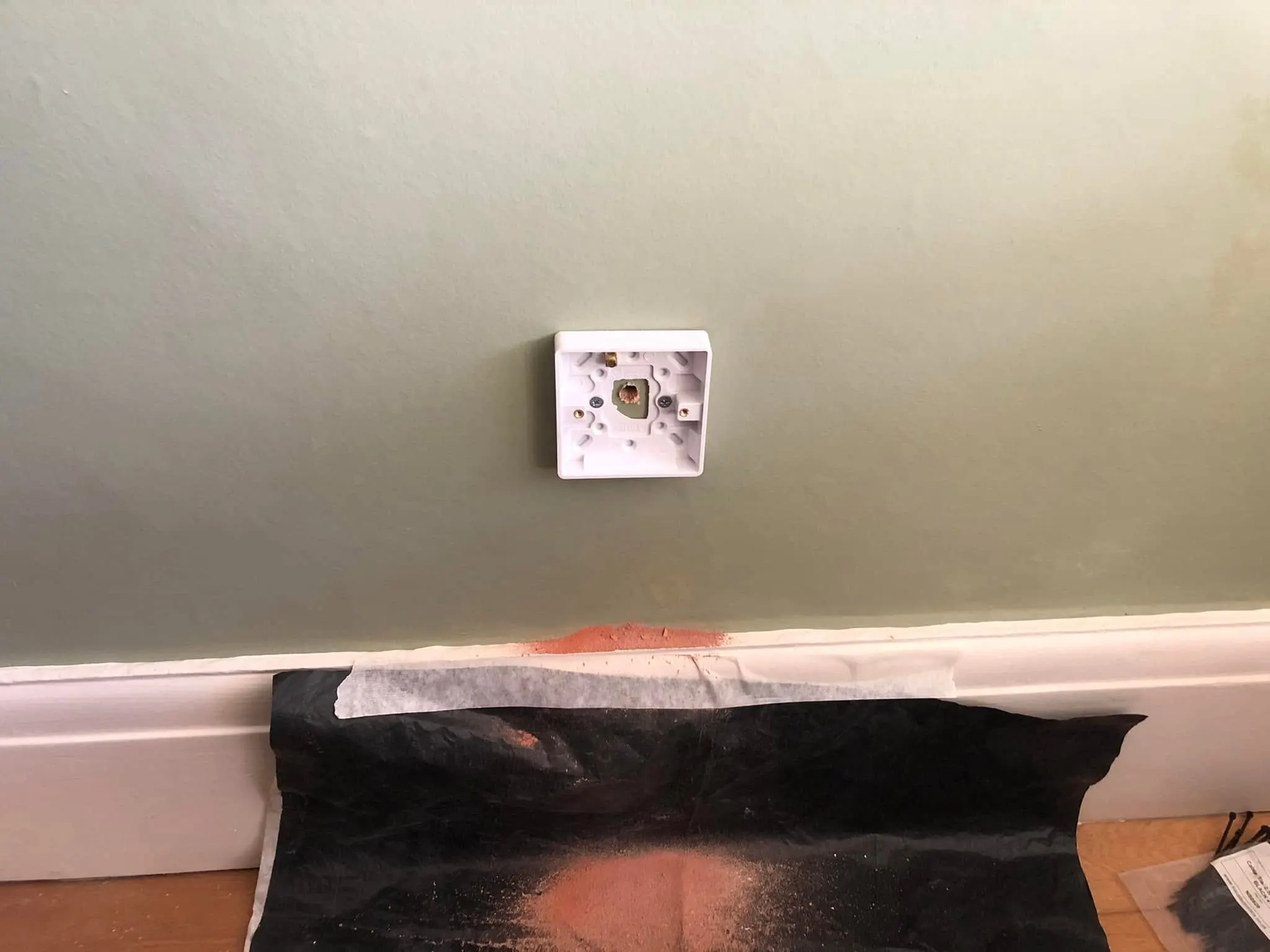Empty white back box on a sage green wall, with brick dust caught on a black sheet taped along the skirting board