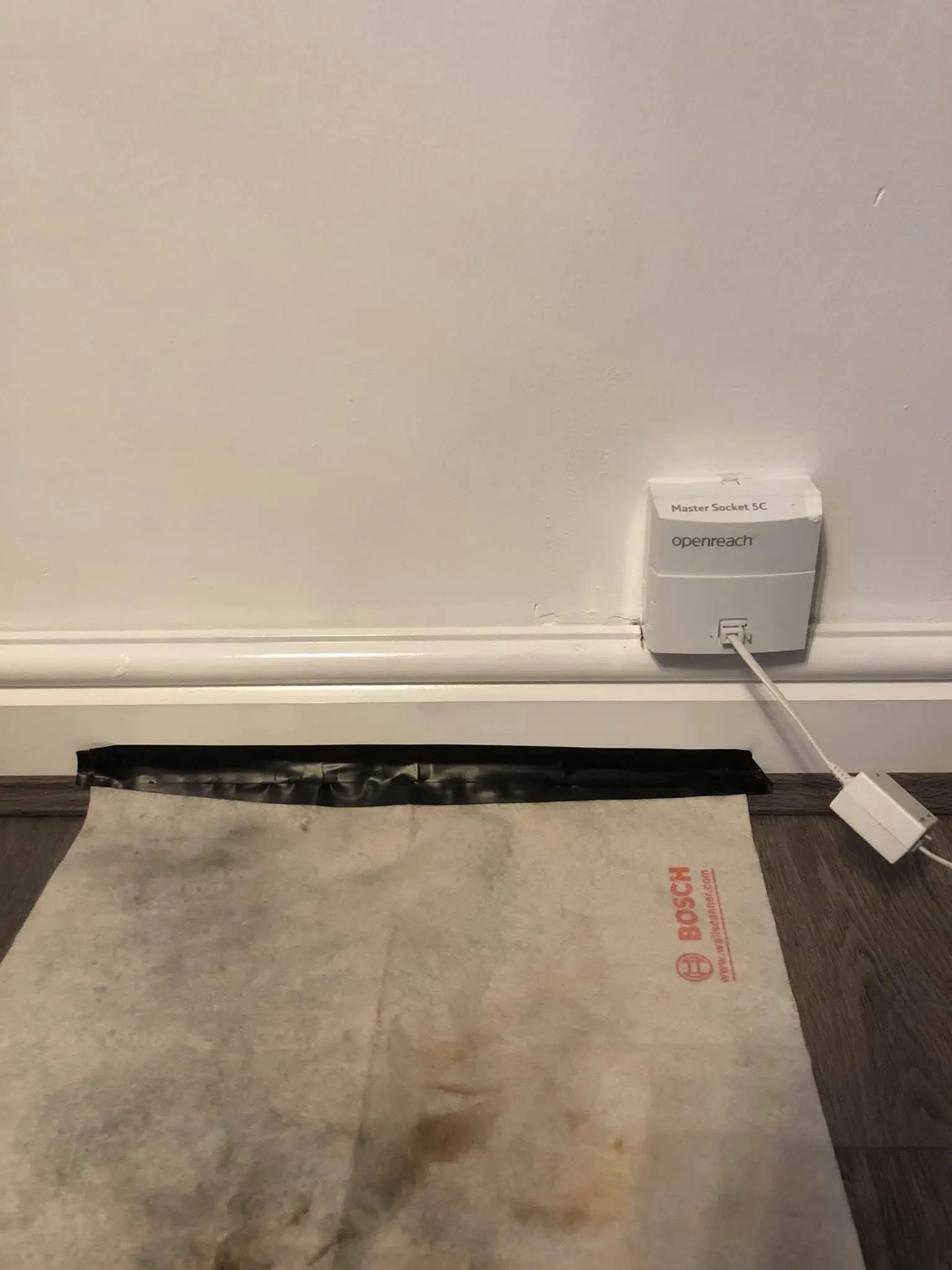 Openreach Master Socket 5C above a white skirting board with a used Bosch dust sheet taped to the floor below
