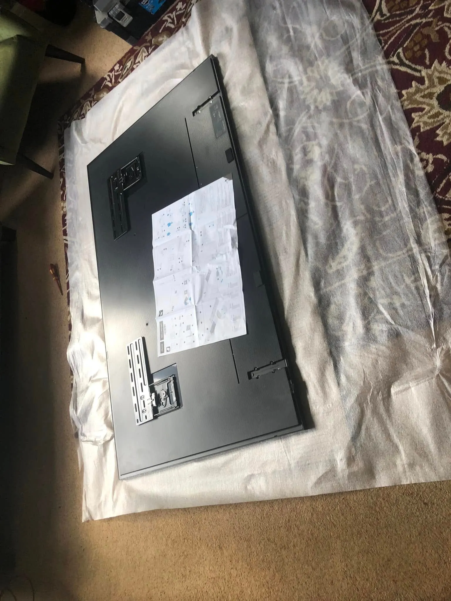 TV lying face down on a white dust sheet with wall-mount bracket plates fixed to its back and the fitting instructions on top